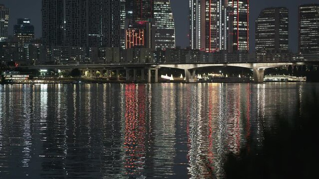 The night time scenery of Yeouido Hangang Riverside in Seoul. Across the Han River on a summer night, you can see a bridge, skyscrapers, and the city lights reflecting on the surface of the river.
