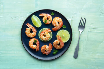 Shrimps, overhead flat lay shot. Fried shrimp with limes on a blue plate, shot from the top on a teal table, with a fork
