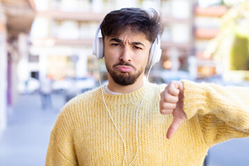 young handsome man feeling cross,showing thumbs down. listening music with headphones