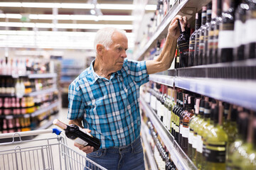 elderly retired senor buying wine in the alcohol section of the supermarket