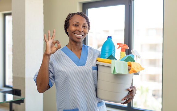 black afro woman feeling happy, showing approval with okay gesture with clean products. housekeeper concept