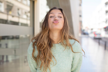 pretty hispanic woman pressing lips together with a cute, fun, happy, lovely expression, sending a kiss