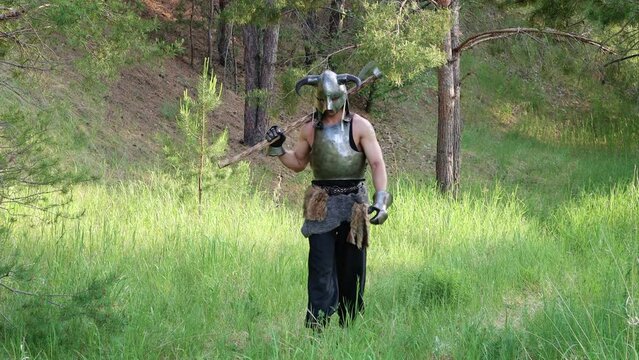 Smooth camera movement, selective focus. A warrior in a horned helmet, a steel breastplate with a two-handed ax in his hands, walks through the forest.