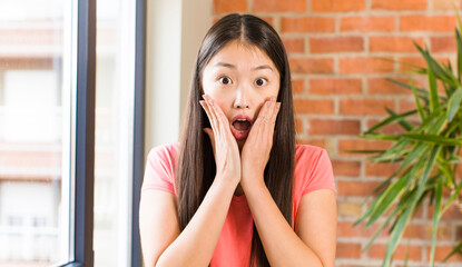 asian pretty woman at home against brick wall with a plant