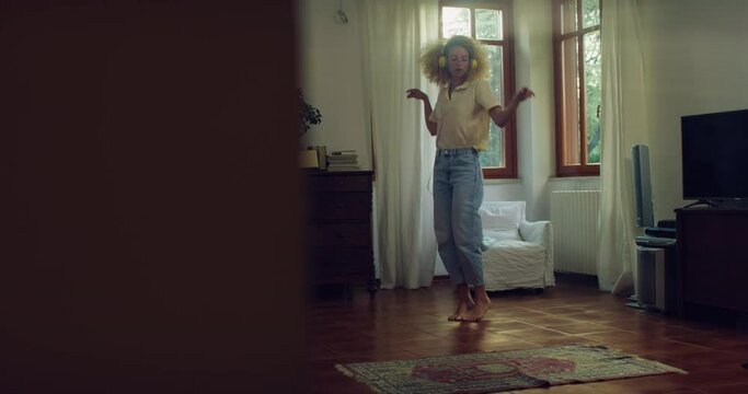 Wide Shot Portrait of Beautiful Brazilian Girl with Curly Hair Using Headphones to Listen to Music and Dance in her Apartment on a Sunny Day. Slow Motion of Female Dancer at Home Practicing 