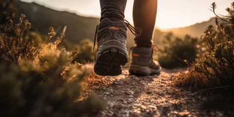 Fotobehang Man hiking up a mountain trail with a close-up of his leather hiking boots. The hiker shown in motion, with one foot lifted off the ground and the other planted on the mountain trail. Generative AI © Bartek