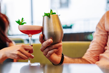 hands of man and women holding and clinking glasses cocktails in restaurant