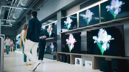 Young Female Shopper Having Conversation with Electronics Store Sales Rep. Stylish Lady Explores Sleek Flat-Screen TV Options. Customer Seeking Impressive Television Solutions in Modern Retail Store
