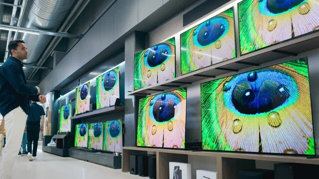 Handsome Young Man Shopping for a TV Entertainment System in a Home Electronics Store. Multiethnic Customer Comparing Different Cinematic Video and Sound Features, Sale Prices and Screen Technology