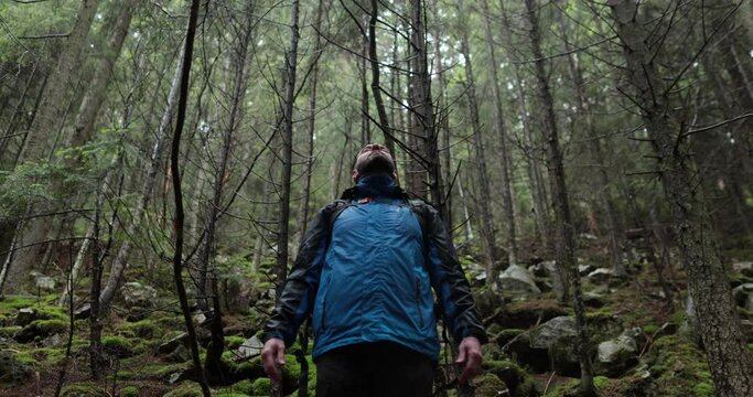 Portrait of a man with a backpack standing in the rain in the forest and raising his hands to the mountain breathing in the mountain air and meditating. The man is alone in the mountains. Hiking among