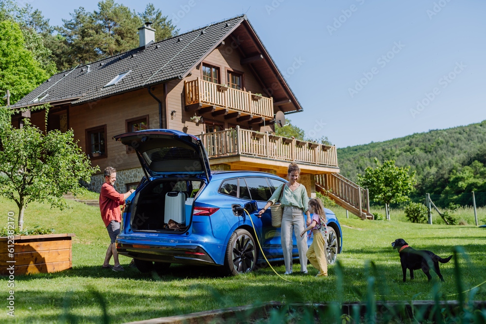 Wall mural Happy family preparing for holiday, charging their electric car.