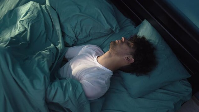 Young man had a terrible nightmare at night, he woke up in horror, looking frightened with open eyes at the camera, top view. Insomnia and mental health
