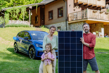 Happy family posing with photovoltaics panel during their electric car charging.