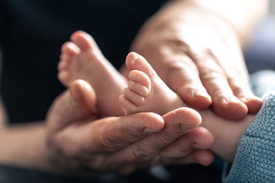 Feet of a newborn baby in the hands of a grandmother, close-up.