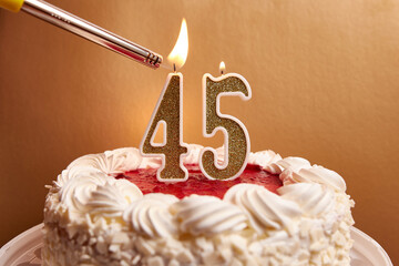 A candle in the form of the number 45, stuck in a festive cake, is lit. Celebrating a birthday or a...