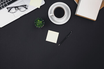Laptop, coffee cups and notepads on a black background, top view.