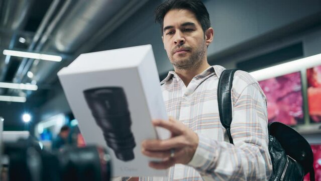 Portrait of a Stylish Hispanic Man Looking at a Box with a Modern Photo Lens, Reading Model's Specifications and Features. Client Shopping for a Camera Zoom Lens in a Home Electronics Store