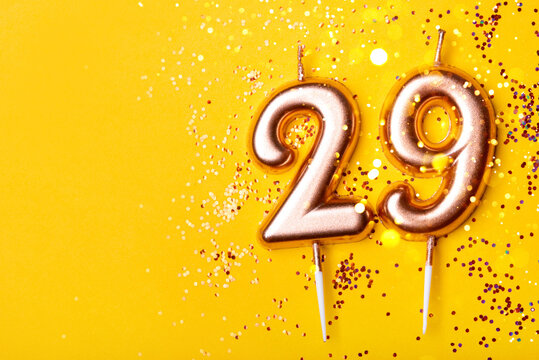 29 years celebration. Greeting banner. Gold candles in the form of number twenty nine on yellow background with confetti.