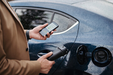 Close up of businessman using electric vehicle charging app, checking charging of his electric car.