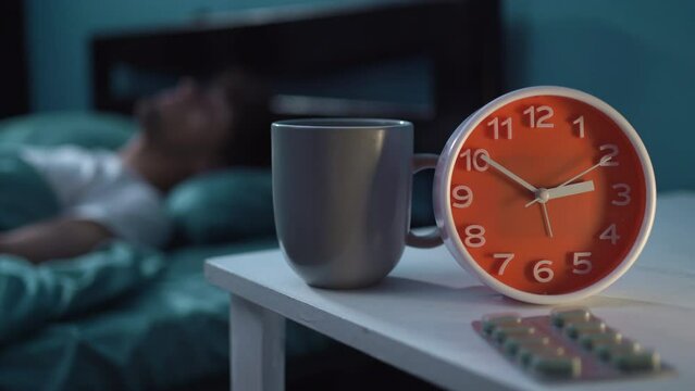 Man at bed take sleeping pill or night medicine. Suffering from insomnia. Cup of water on nightstand in bedroom.