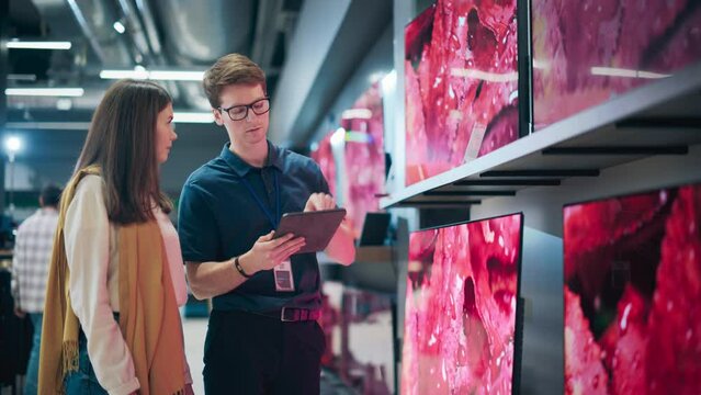 Portrait of a Female Customer Seeking Advice from Retail Home Electronics Expert. Young Lady Explores Modern TV Options. Shopper Evaluating Latest Television Innovations in Elegant Department Store