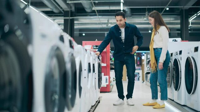 Multicultural Couple Evaluates Washing Machine Choices at Home Electronics Store. Man and Woman in Search of a Reliable Laundry Appliance. Customers Explore Modern Laundry Solutions in a Retail Shop