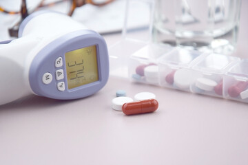 Calendar with pills and non-contact thermometer on light background.