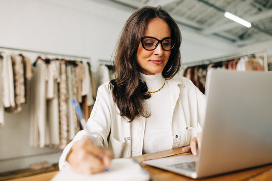 Small Business Plans: Woman Using A Laptop As She Brainstorms In Her Clothing Shop