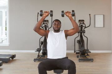 Fototapeta na wymiar Young african american man in muscular sportswear is exercising lifting dumbbells in gym.