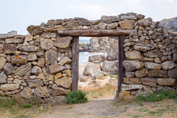 An old dilapidated stone wall with a doorway overlooking the sea and the rocky shore. Film decoration