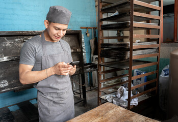 A young Hispanic baker is having a break to use the phone in the bakery