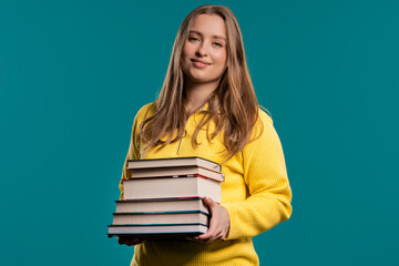 Smiling adult student woman with stack of books from library on blue background