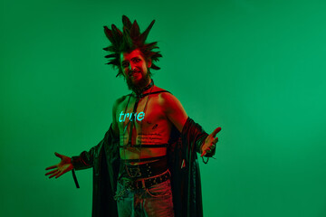 Fototapeta premium Expressive young man, rock musician, punk with neon filter on body posing against green studio background in neon light. True. Concept of music, lifestyle, subculture, art, youth, human emotions