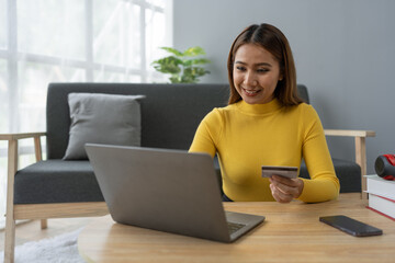 Naklejka premium Business woman, young woman holding credit card and using laptop computer for online shopping, e-commerce, banking, internet application, spending money, working from home startup business ideas