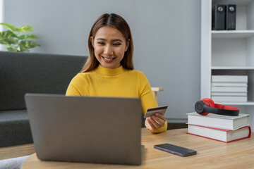 Fototapeta premium Business woman, young woman holding credit card and using laptop computer for online shopping, e-commerce, banking, internet application, spending money, working from home startup business ideas