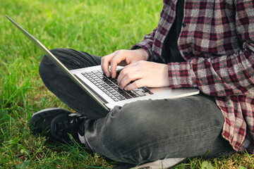 Man in the park sitting on the grass with a laptop, close-up hands and laptop.