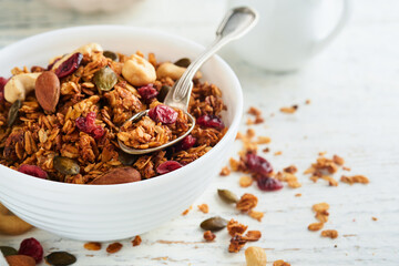 Homemade granola in glass jar with greek yogurt or milk and cashews, almonds, pumpkin with dried cranberry seeds in on white rustic wooden table background. Healthy energy breakfast or snack. Top view