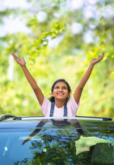 Vertical shot of happy teenager girl kid feeling nature by raising hands on car sunroof - concept...