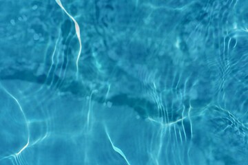 Blue water with ripples on the surface. Defocus blurred transparent blue colored clear calm water surface texture with splashes and bubbles. Water waves with shining pattern texture background.