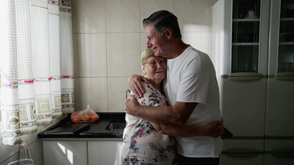 Adult son embracing elderly mother standing at home kitchen. Authentic real people lifestyle. Man...