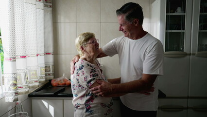 Adult son embracing elderly mother standing at home kitchen. Authentic real people lifestyle. Man...