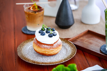 Close up and selective focus donut with cream and blueberries in plate on wooden table. 