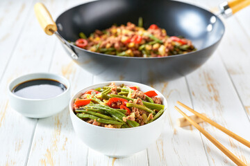 chinese cuisine sichuan stir-fried green beans in a wok with pork, garlic, hot pepper, ginger on a wooden table.