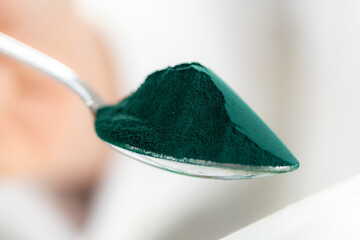 Spirulina spoonful close-up. Spoon filled with nutrient-rich superfood spirulina with its vibrant...