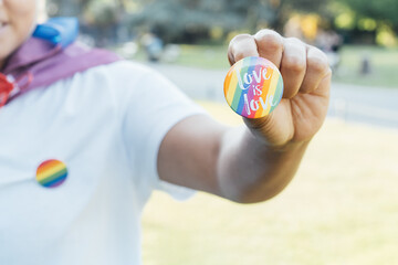 Closeup of LGBTQ rainbow flag pin in the hand of young lesbian activist. Round badge with Love is...