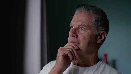 Middle-Aged Man with Gray Hair Gazing Out Window with hand in chin, Contemplative Expression Suggesting Deep Thought about Life