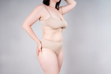 Fat woman in beige underwear on gray background, overweight female body