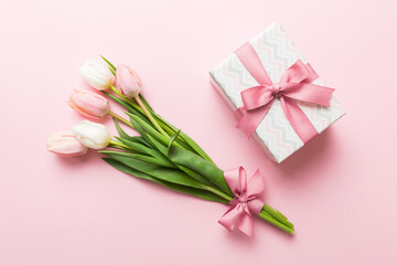 Pink tulips flowers and gift or present box on colored table background. Mothers Day, Birthday, Womens Day, celebration concept. Space for text top view