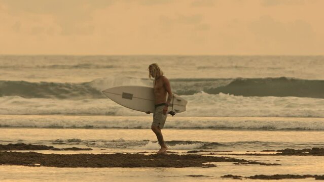 Cinematic tired exhausted drained jaded caucasian man bodyboarder goes after bodyboarding workout from big epic ocean waves. Concept fatigue after sports workout, exhaustion after bodyboarding session
