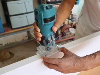 Close-up of a carpenter's hand working with a manual electric trimmer in a home workshop. 